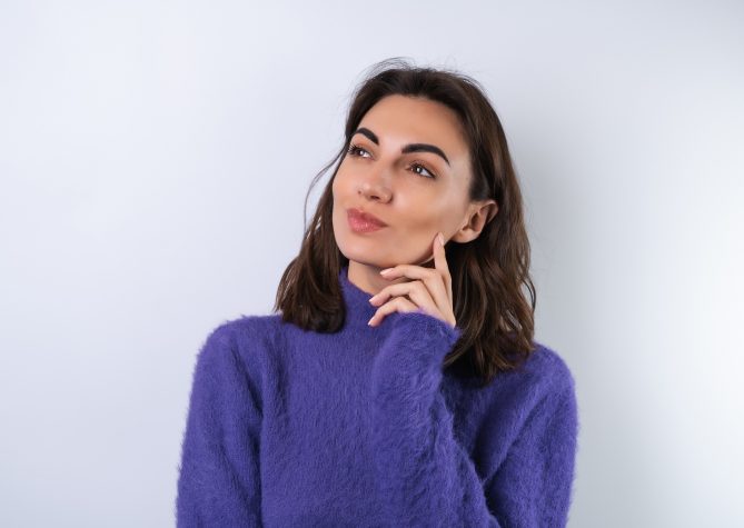 Young woman in a purple soft cozy sweater on the background thoughtful, thinking  of ideas look aside