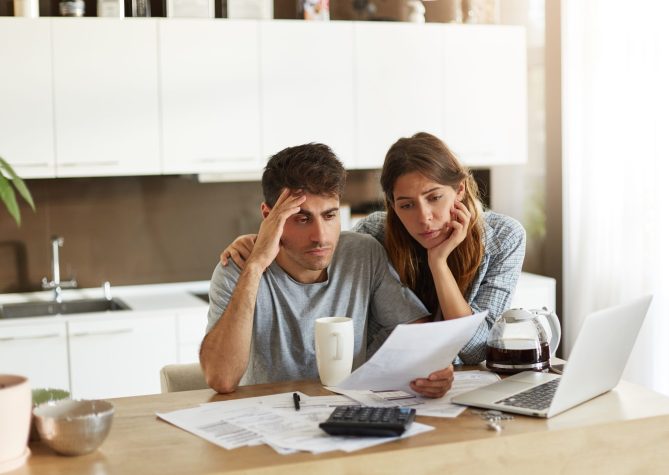 Unhappy American couple managing home accounts in kitchen, trying to save some money by cutting family expenses. Finances, bankruptcy, taxes, money, accounting and financial problems concept